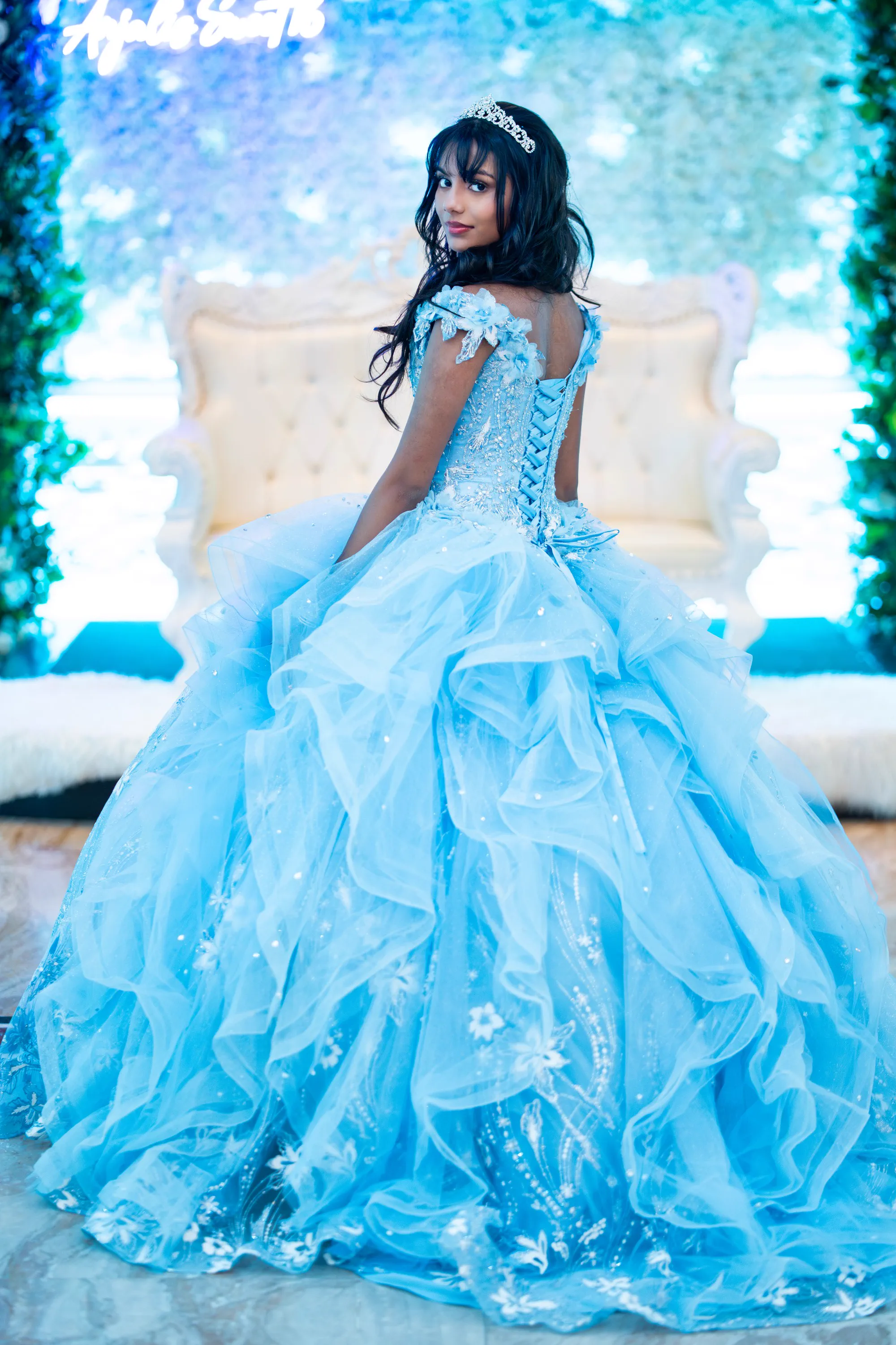 A Sweet 16 celebrant in a voluminous blue gown looks back toward the camera.