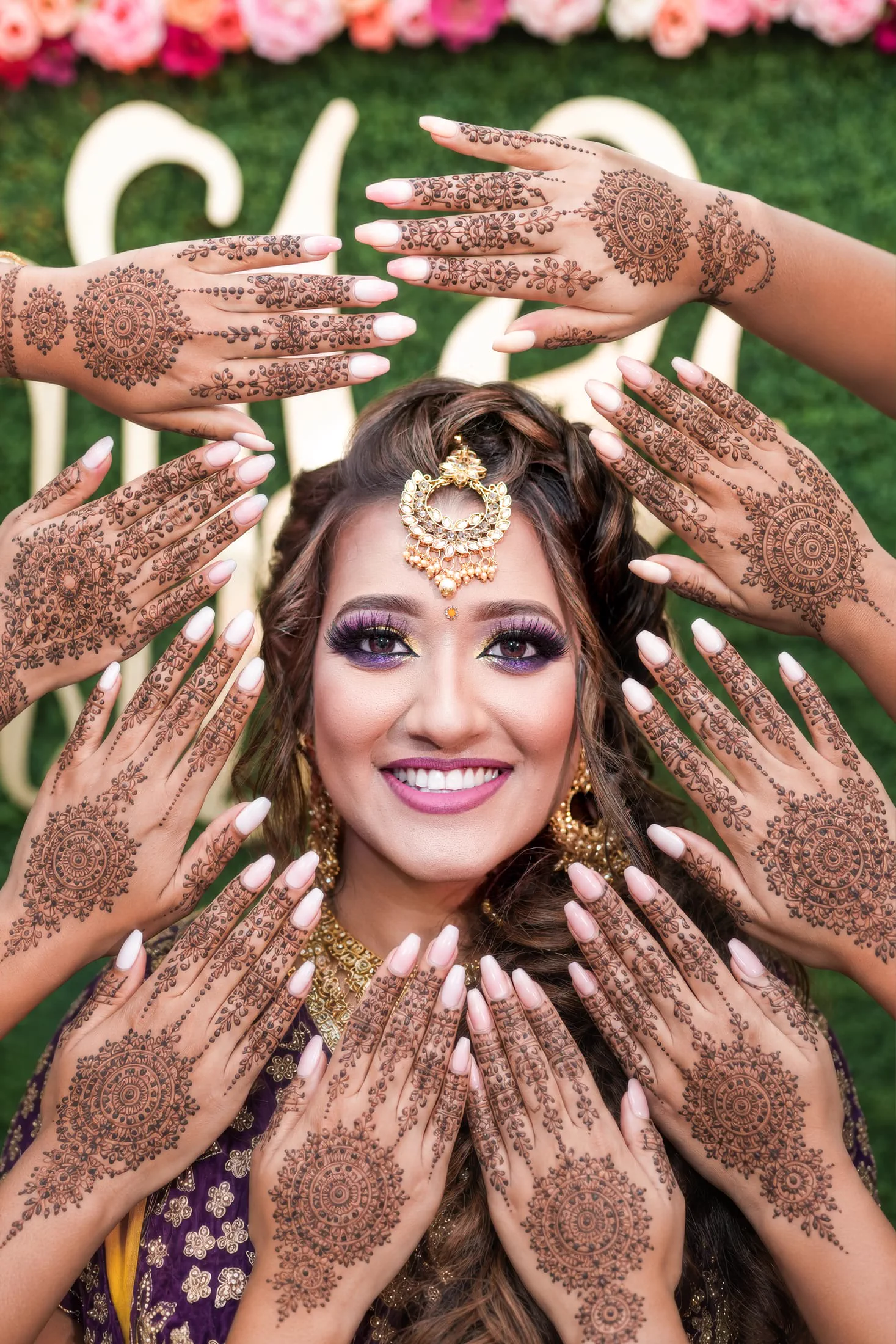 A bride's face framed by intricately hennaed hands.
