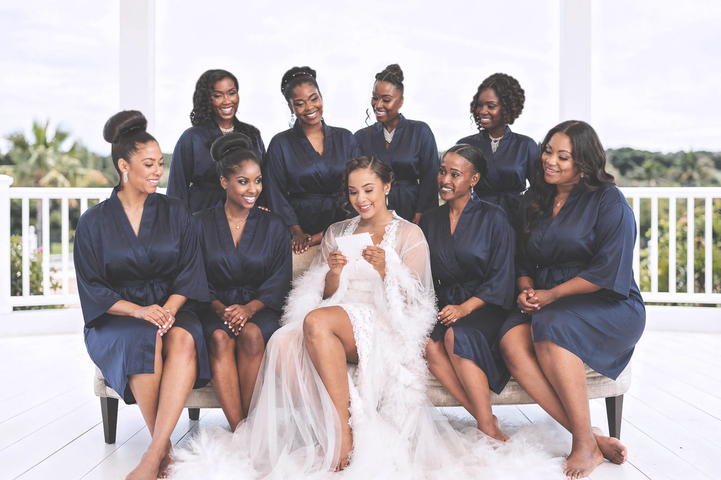 A bride reads a card surrounded by eight bridesmaids in matching navy robes.