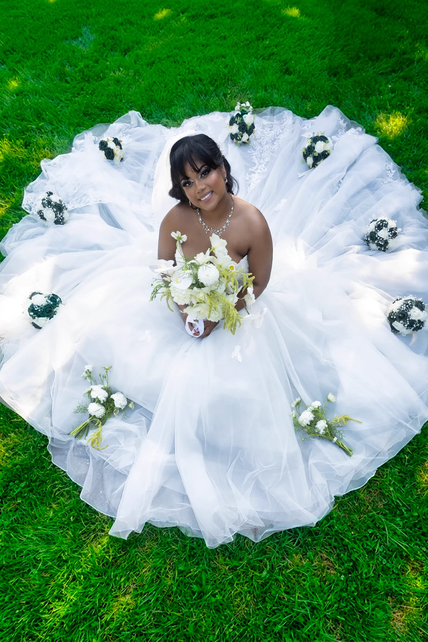 An aerial view of a bride whose gown spreads across the lawn, ringed by bouquets.