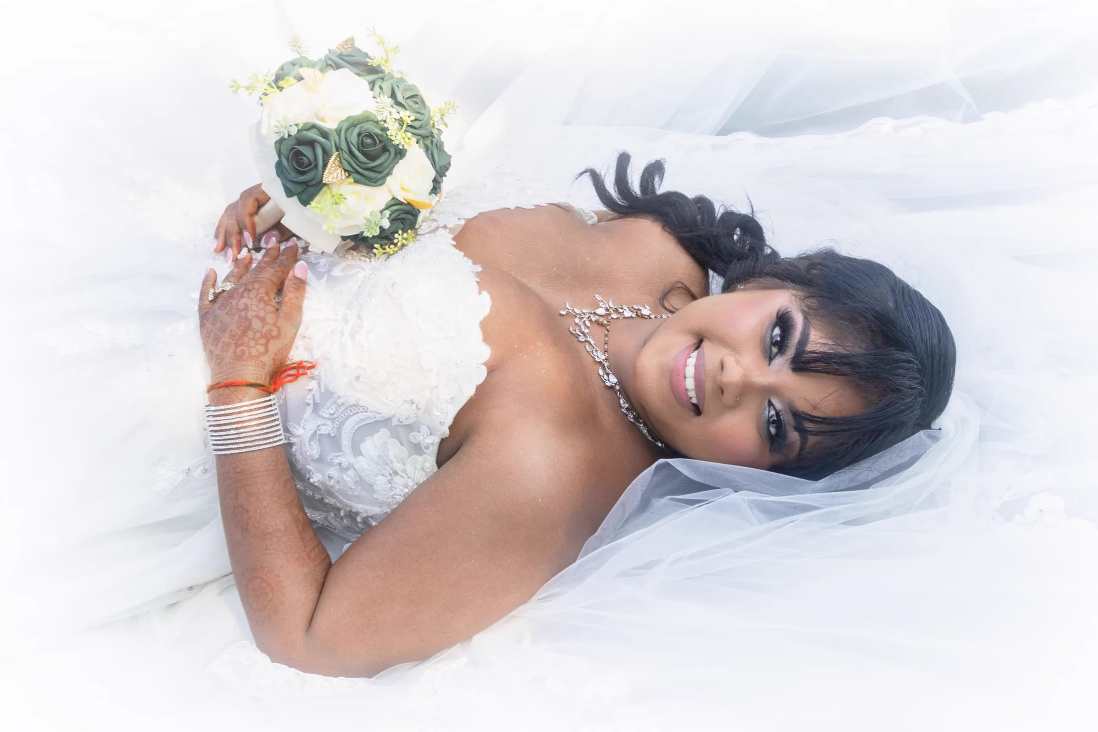 A bride reclines with her bouquet in a dramatic editorial portrait.