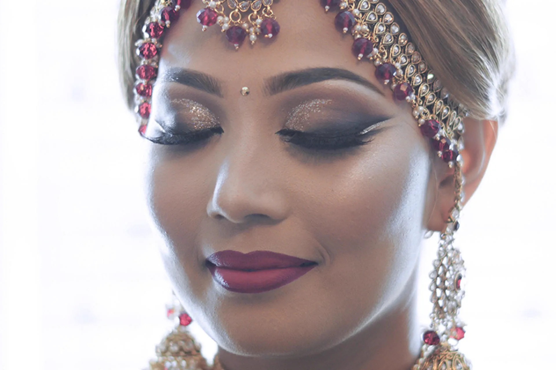 A close portrait of a bride's jeweled headpiece, earrings, and bold makeup.