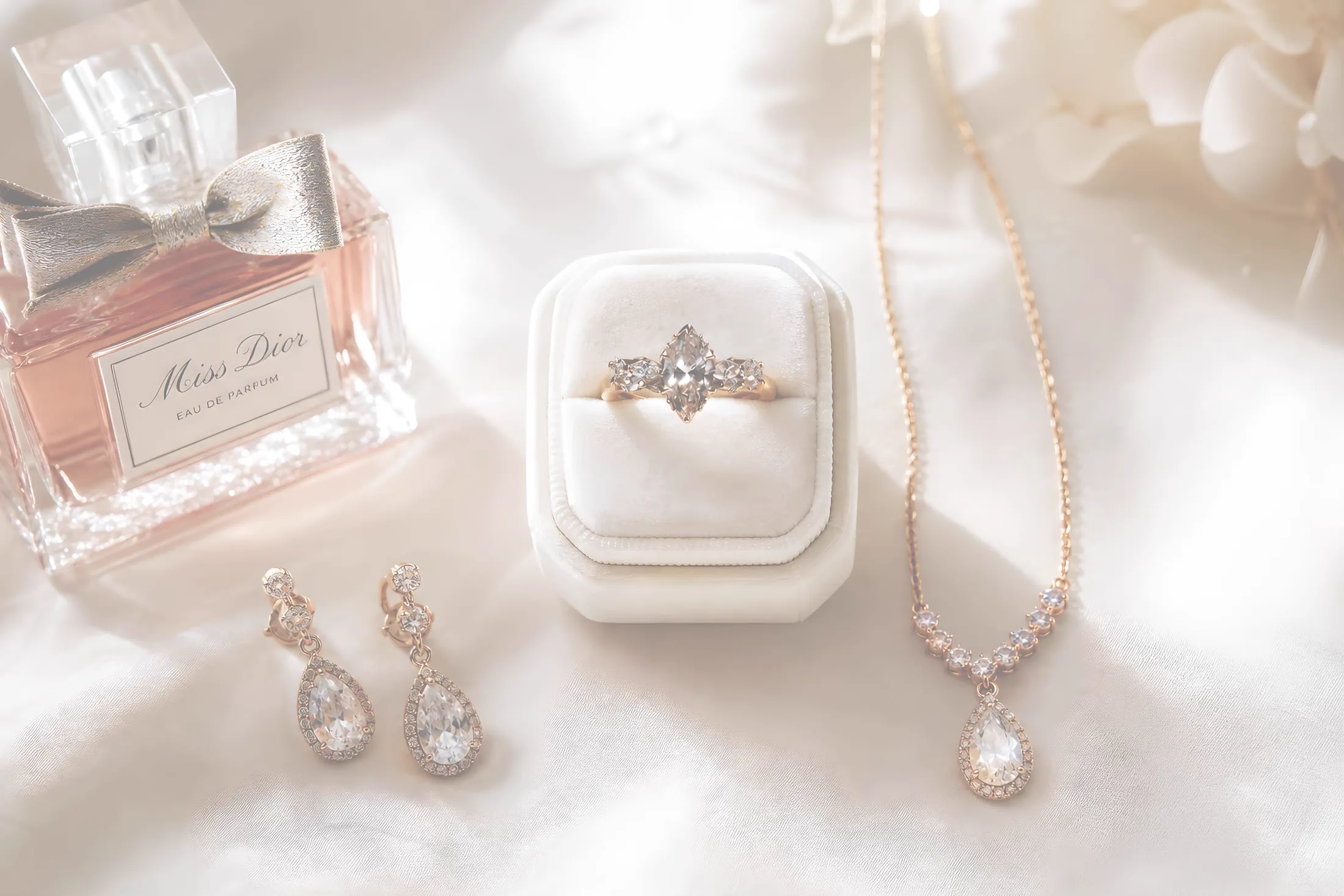 A flat lay of the bride's wedding day details: perfume, engagement ring, earrings, and necklace.