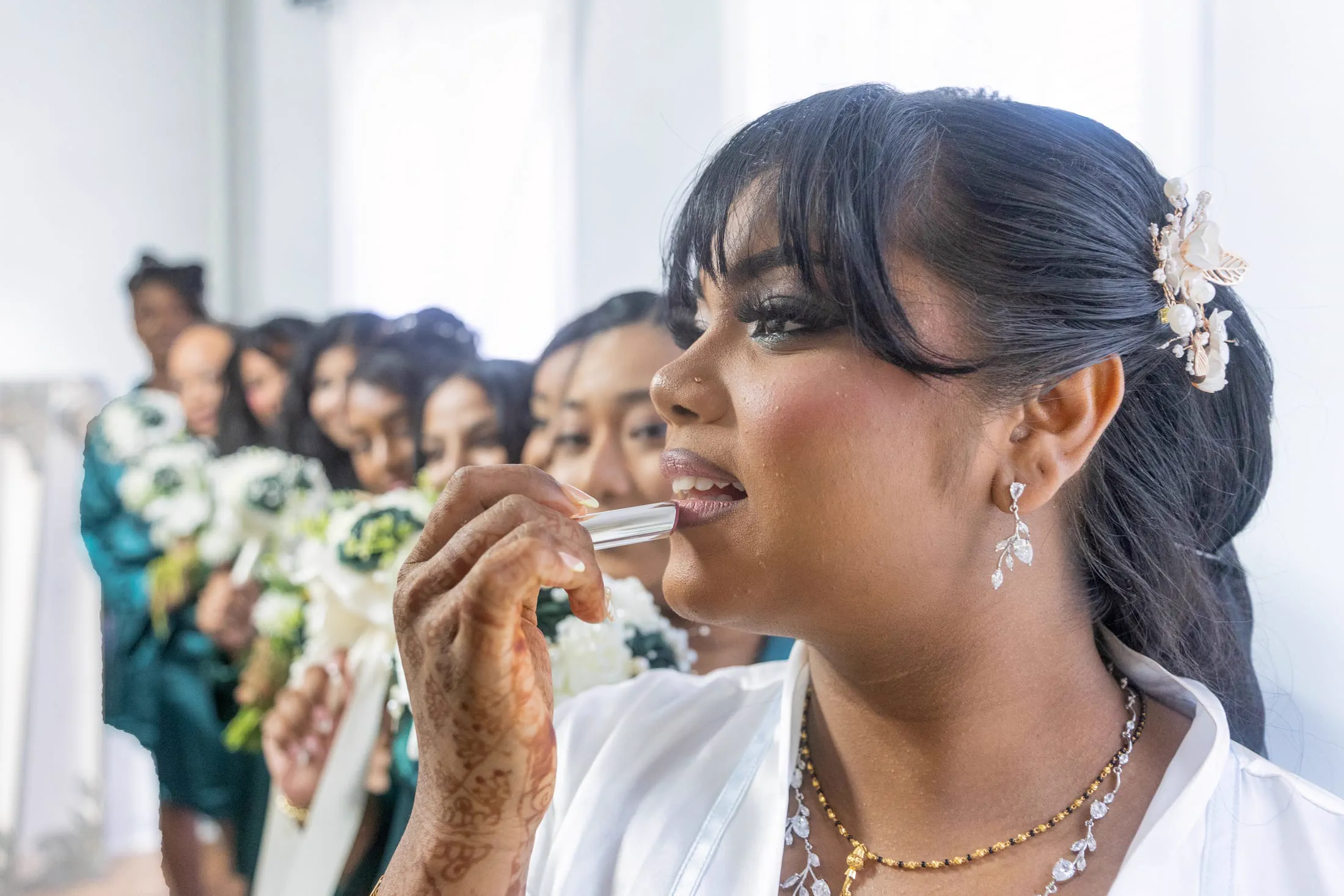 A bride laughs with her bridesmaids in teal robes while getting ready.