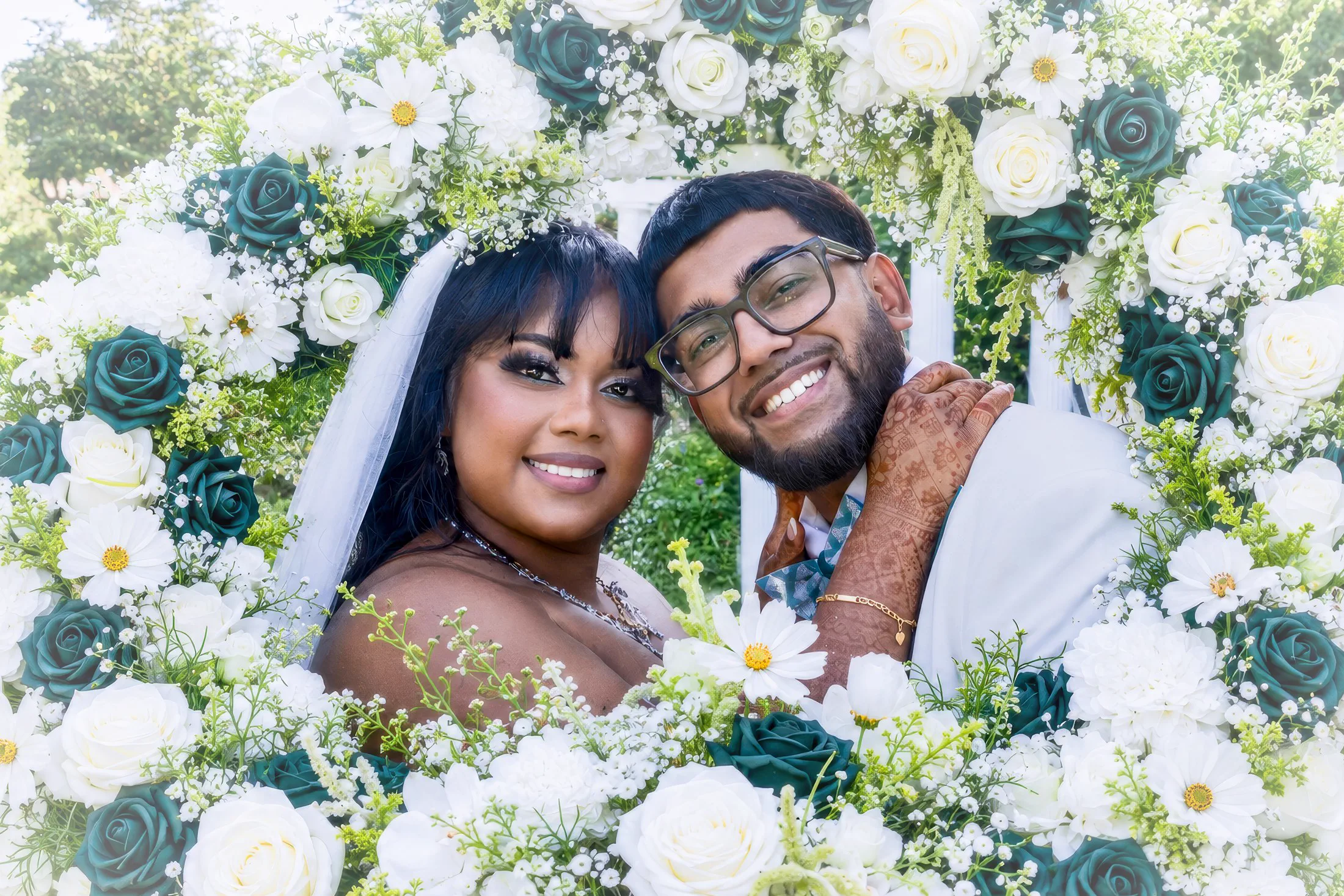 Newlyweds smile together within an abundant floral installation.