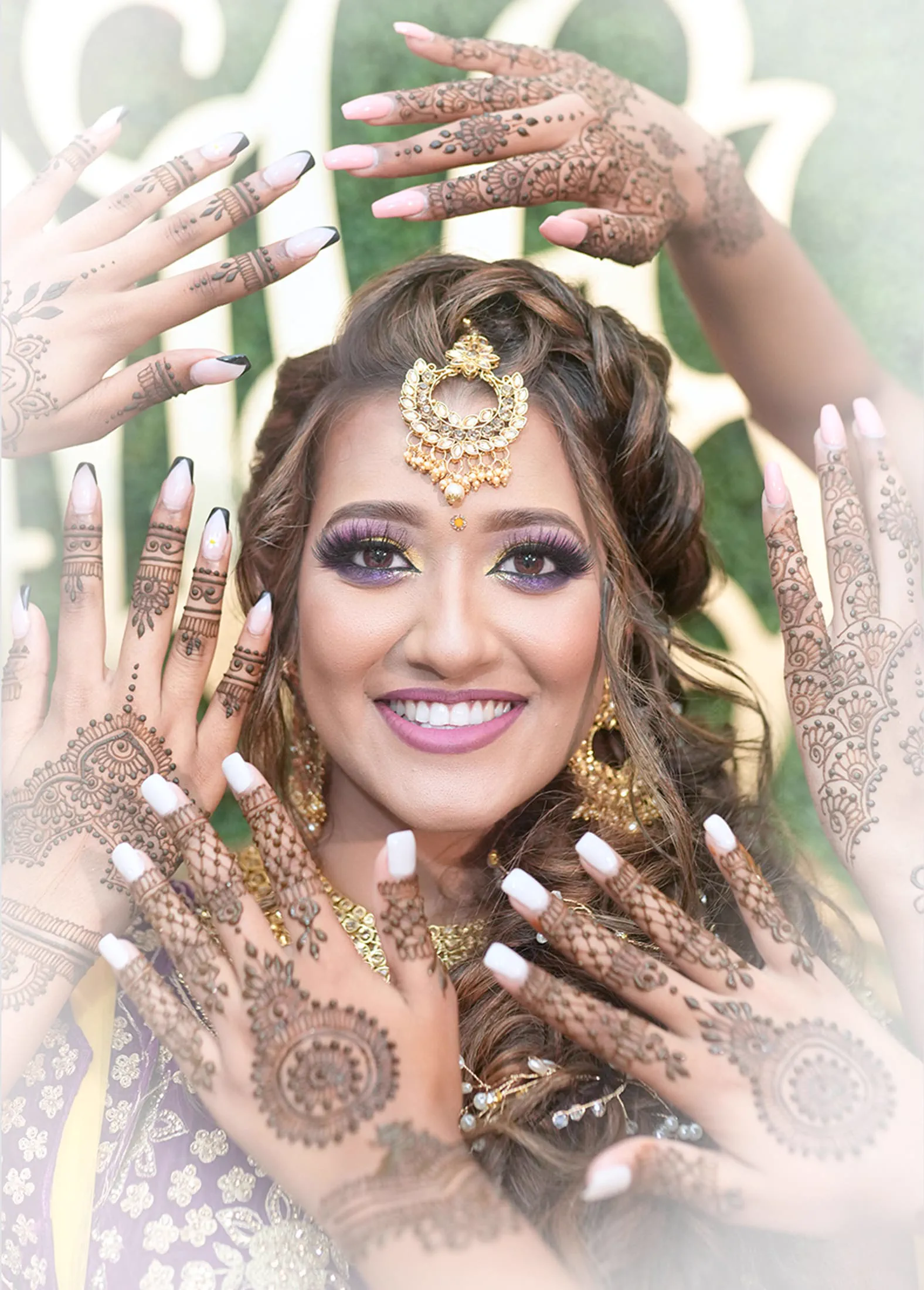 A bride's face is framed by a crown of hennaed hands reaching toward her.