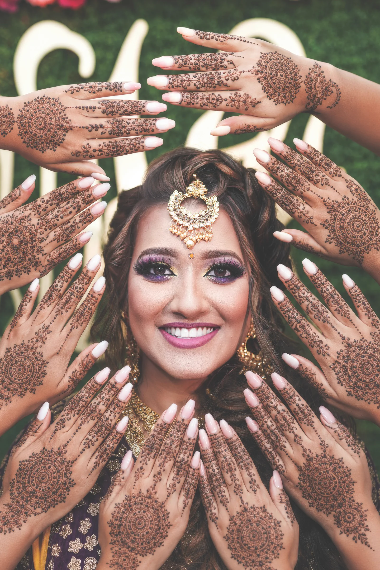 A South Asian bride is framed by a circle of intricately decorated henna hands.
