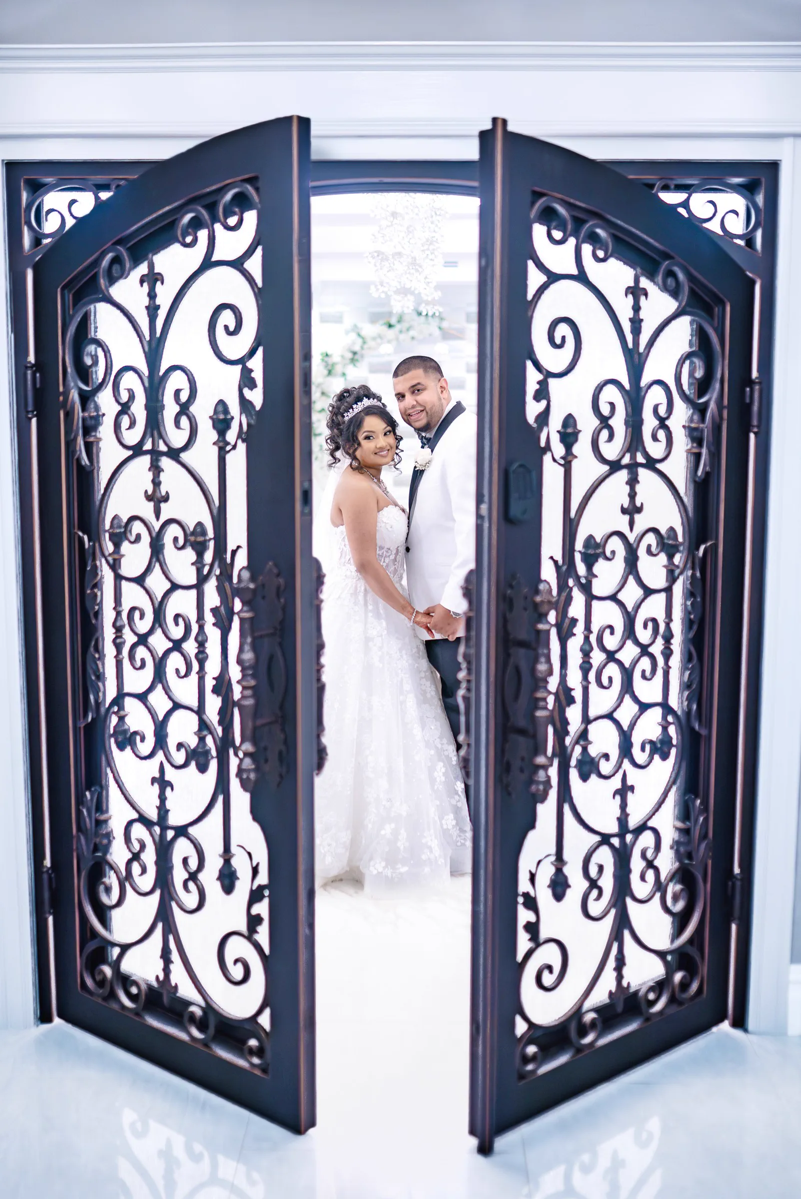 A newlywed couple stand together within ornate iron doors.