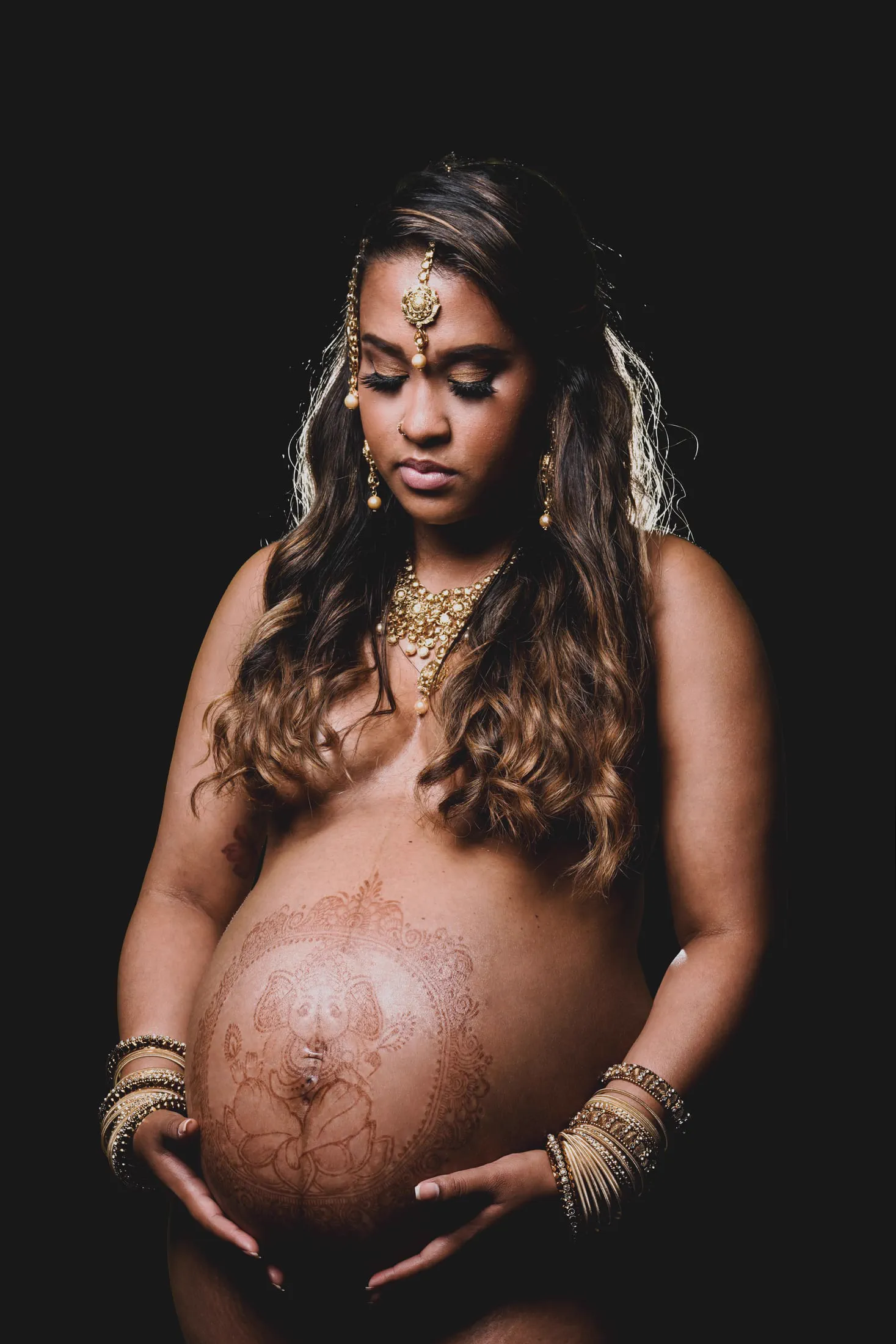A close portrait of an expecting mother's belly, decorated with intricate henna art.