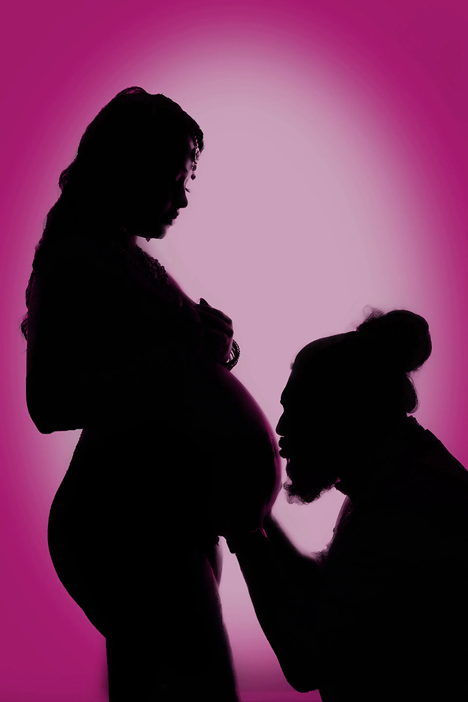 A silhouetted maternity portrait of an expecting couple against a magenta backdrop.