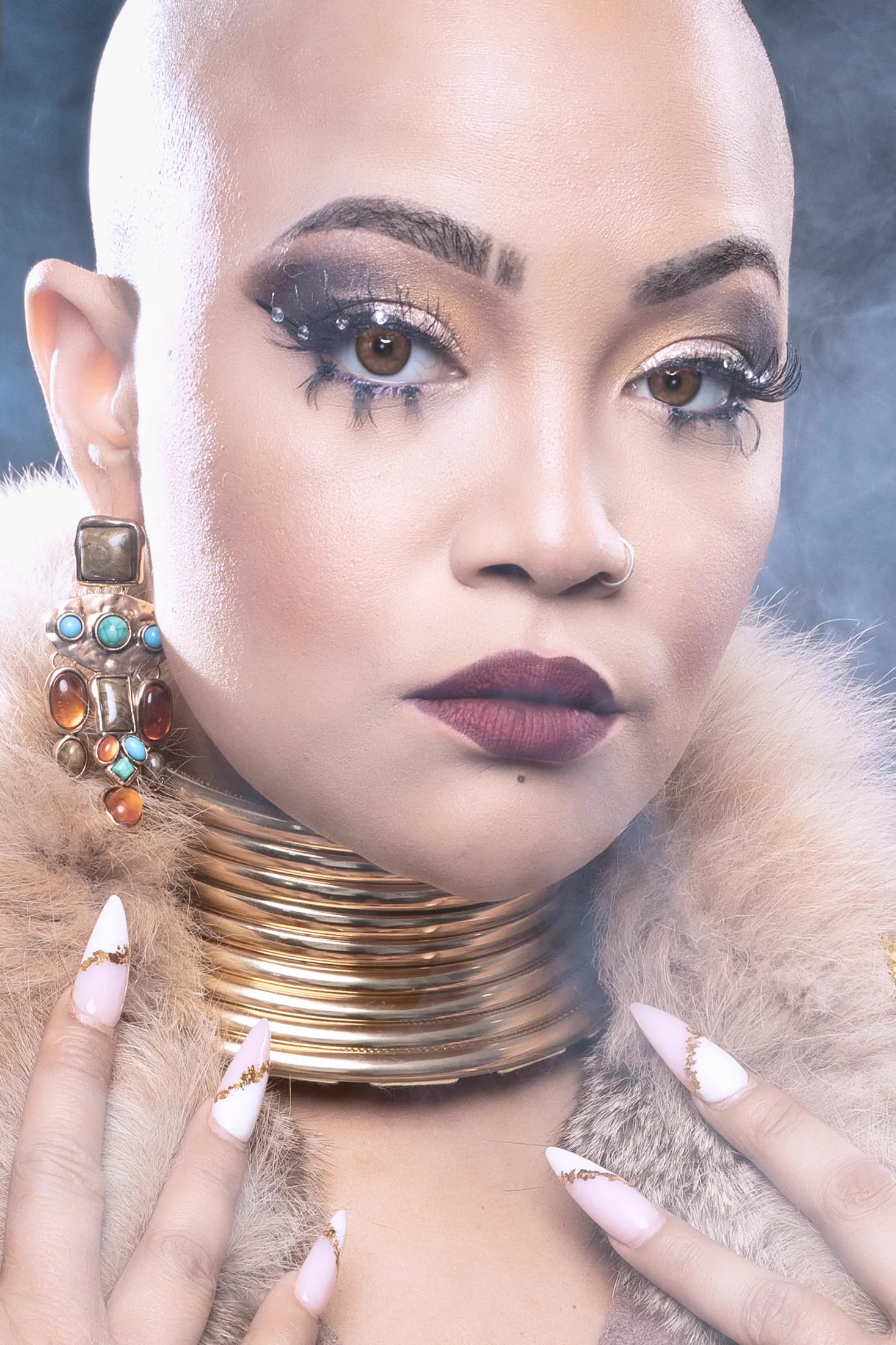 A bald model in a coral off-shoulder top with gold jewelry against a yellow backdrop.
