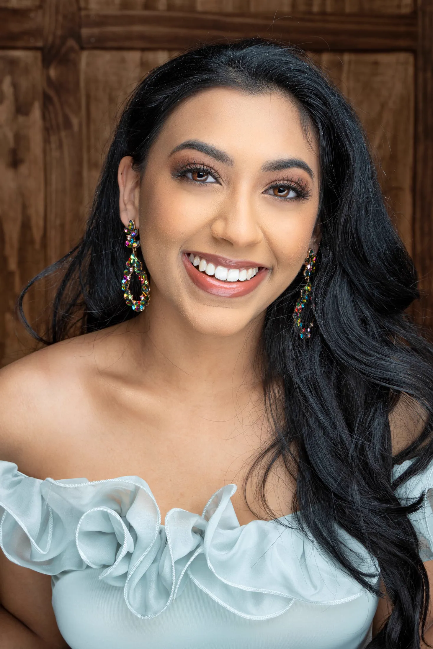 A bright, smiling headshot with colorful jeweled statement earrings.