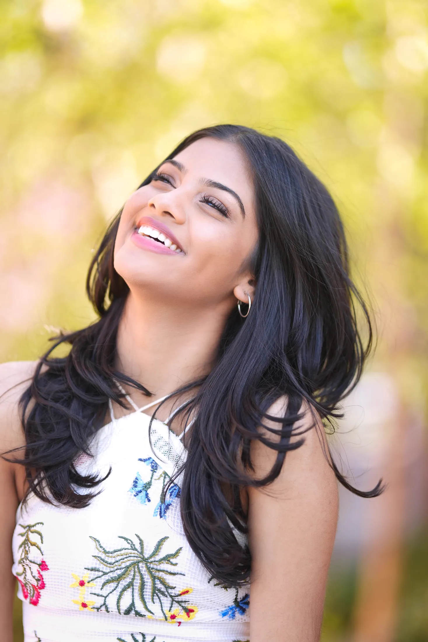 A candid, smiling portrait of a woman in an embroidered floral top outdoors.