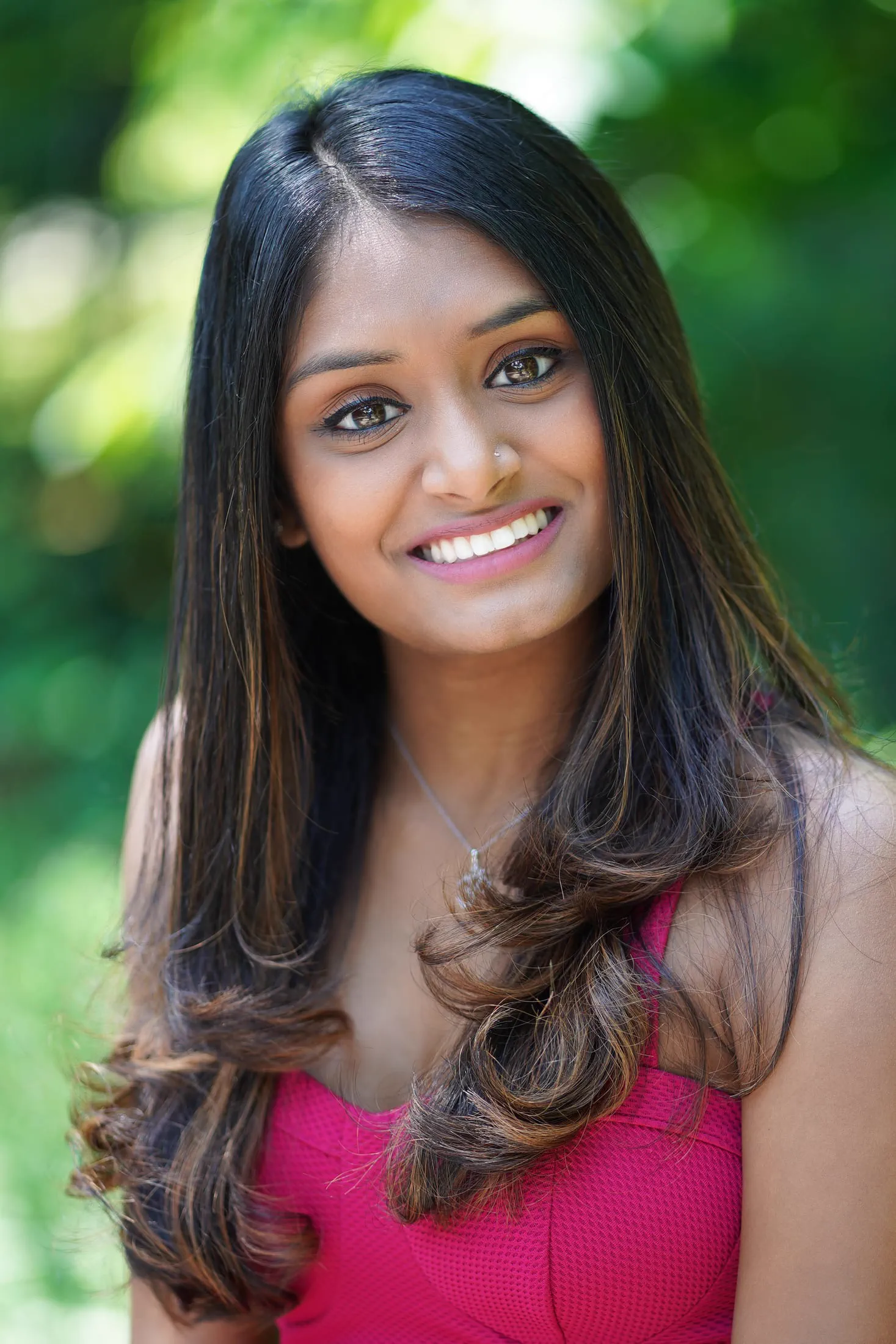 A natural, smiling headshot of a woman in a pink top outdoors.