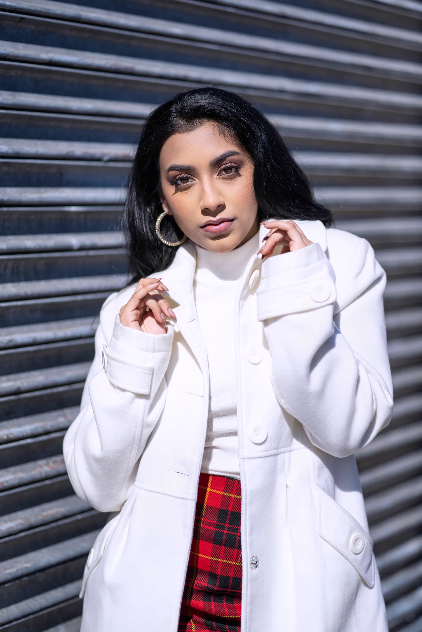 A woman in a white coat and plaid top poses on an industrial staircase.
