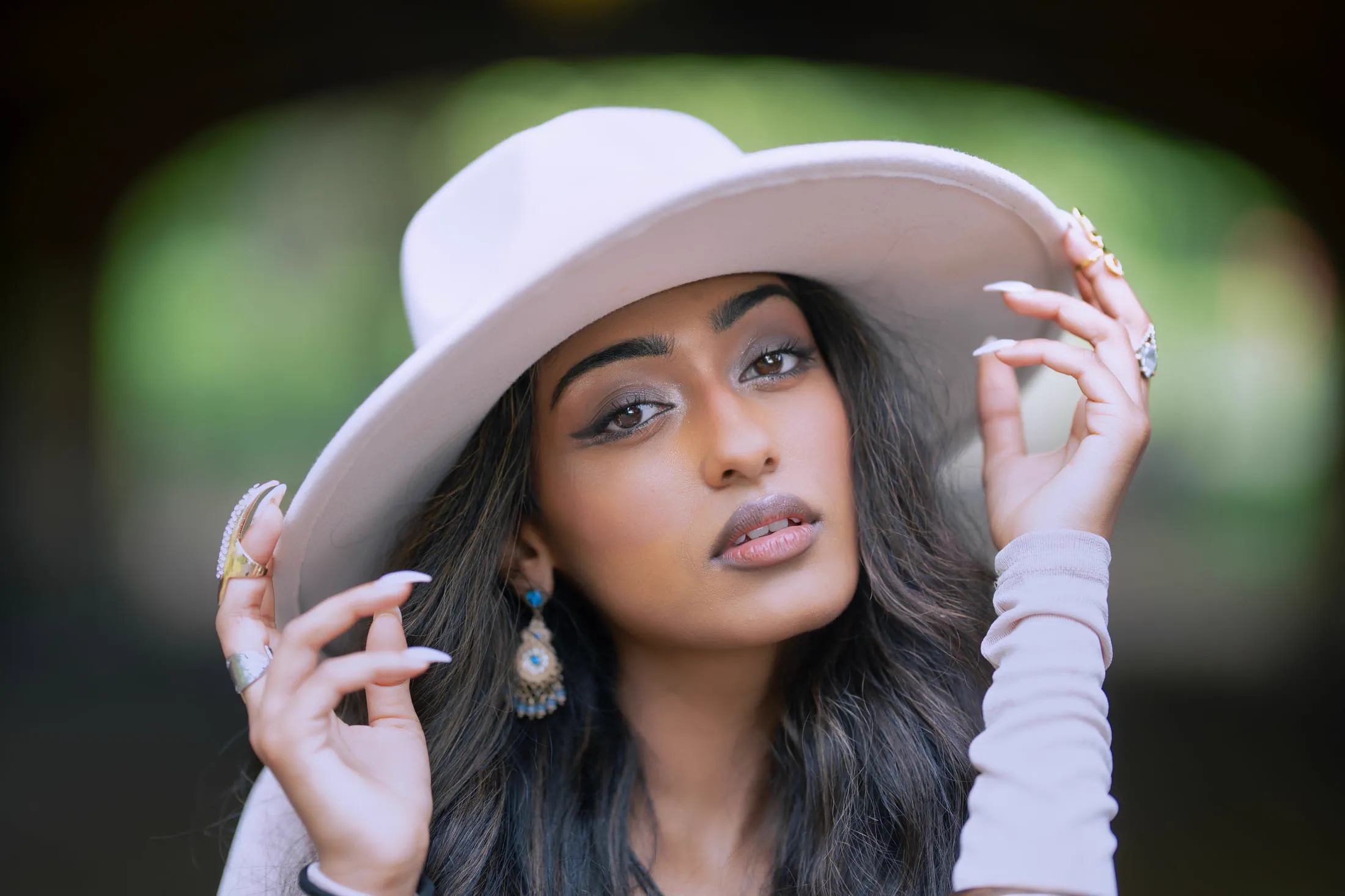 A close portrait of a woman in a wide-brim white hat and beaded earrings.
