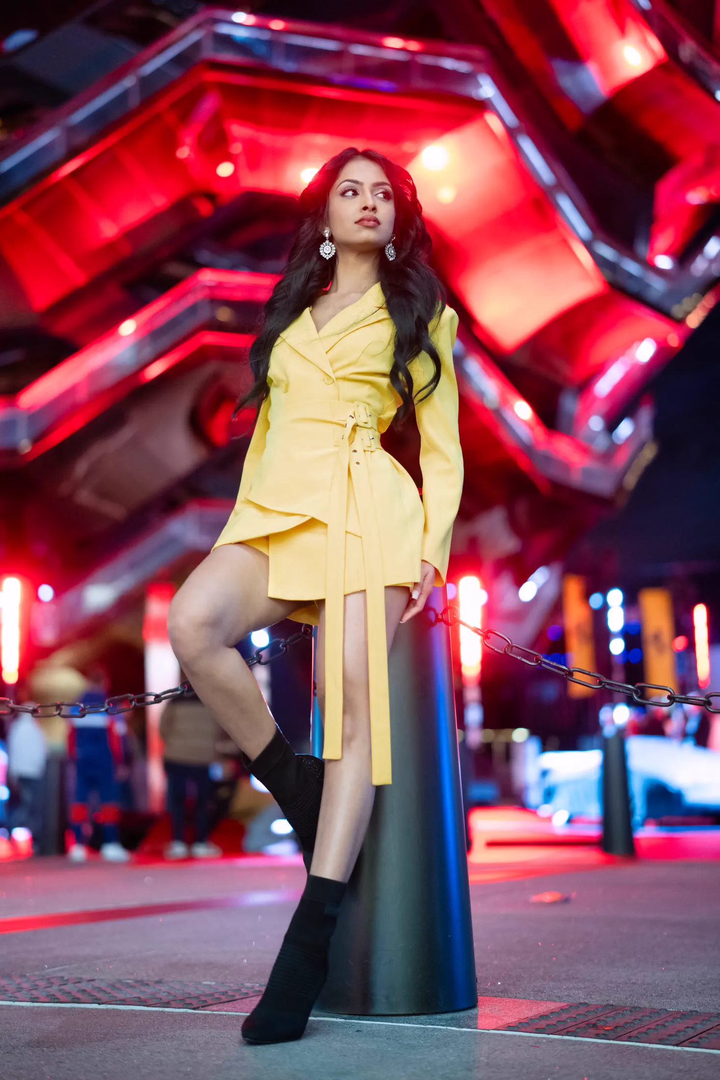 A woman in a yellow dress poses beneath red neon lighting.