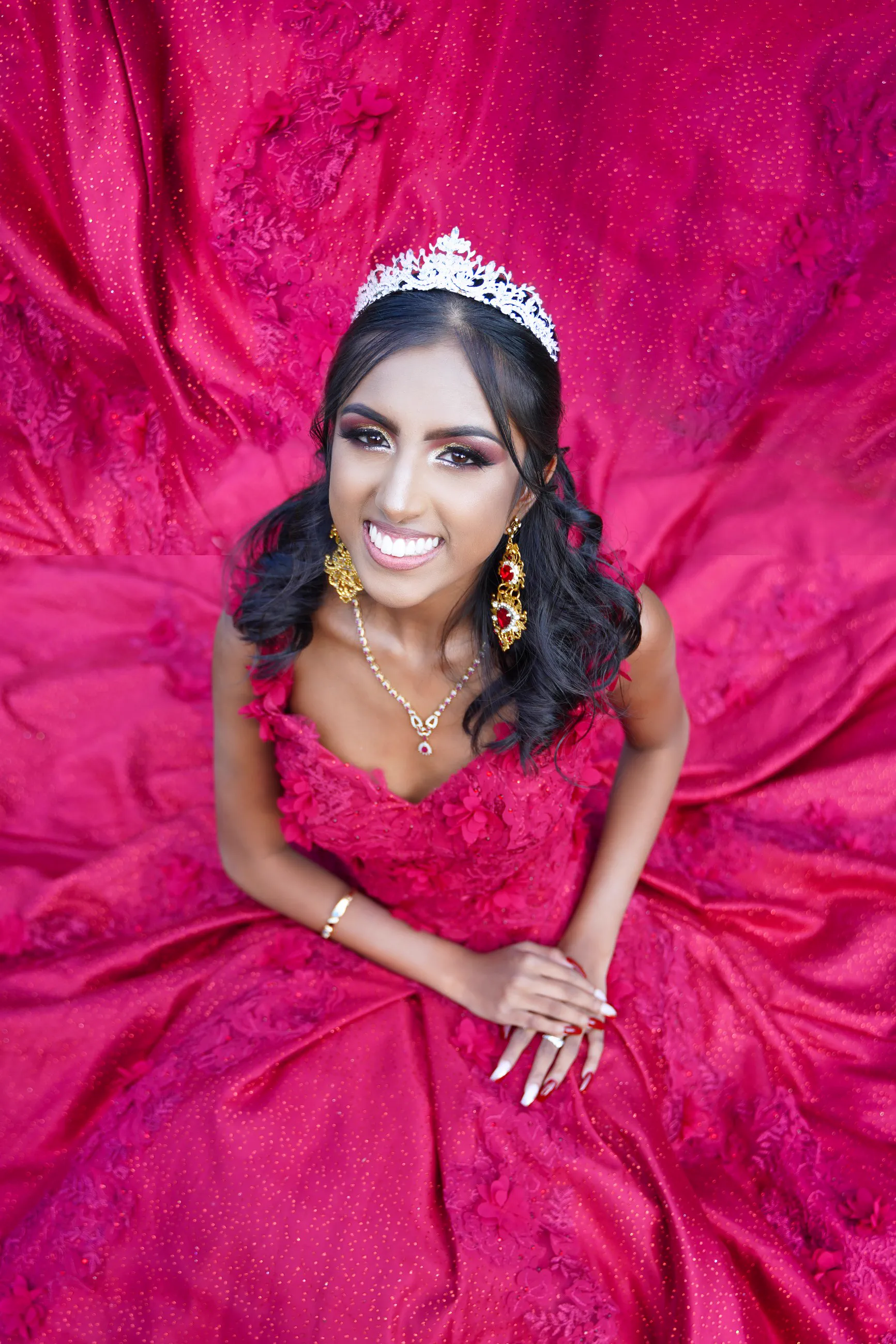 A Sweet 16 celebrant in a crimson gown looks up from a circle of flowing fabric.