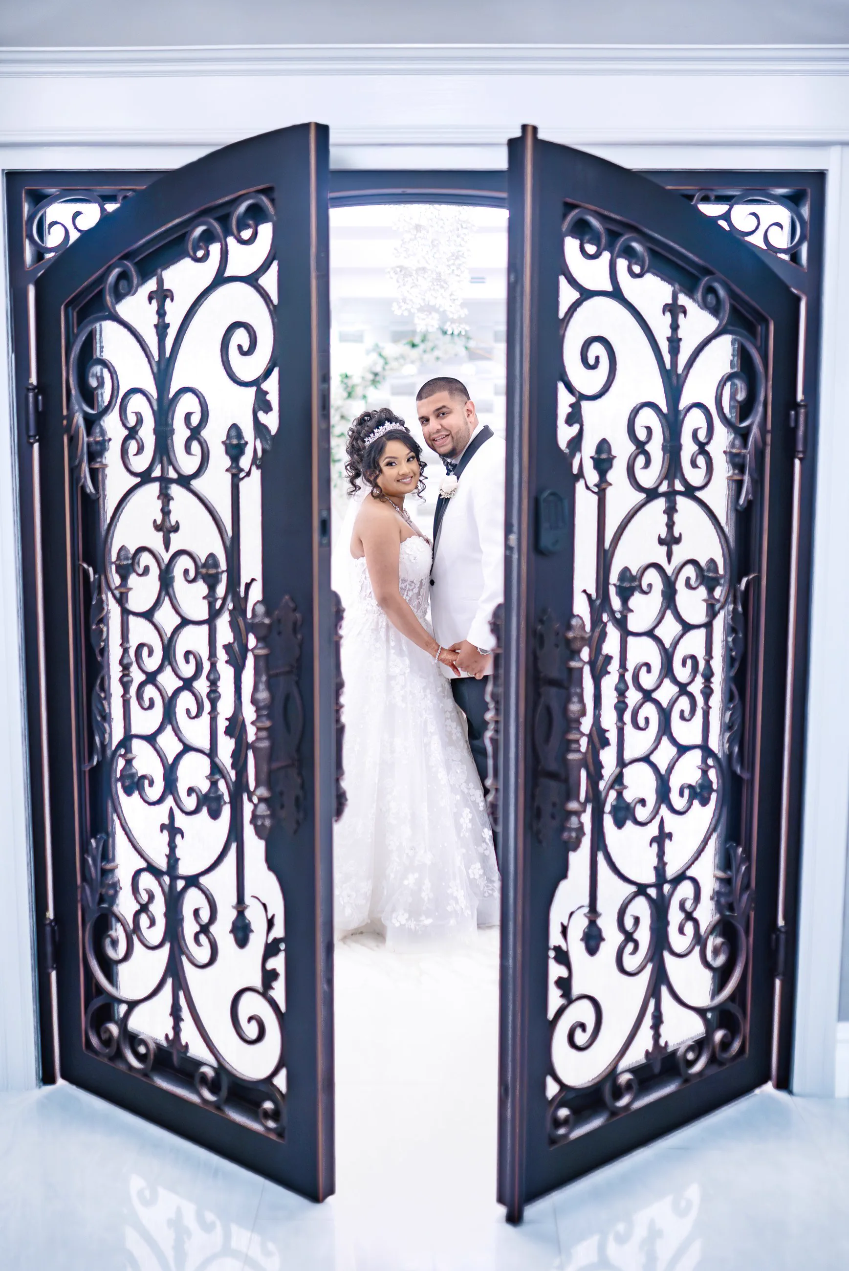 A newlywed couple stand together between ornate iron doors.