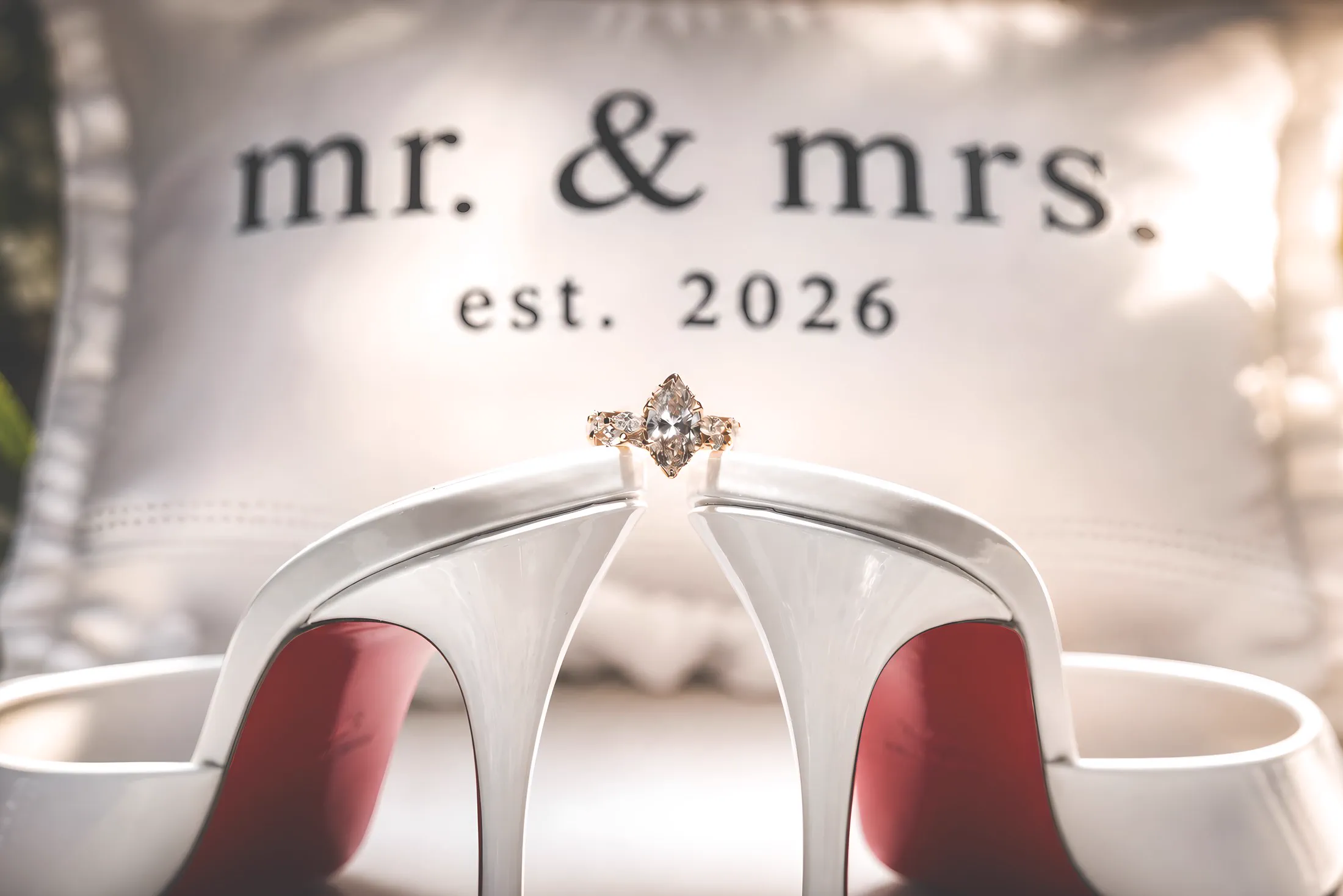 An engagement ring balanced between the bride's heels, with a mr. and mrs. pillow in the background.